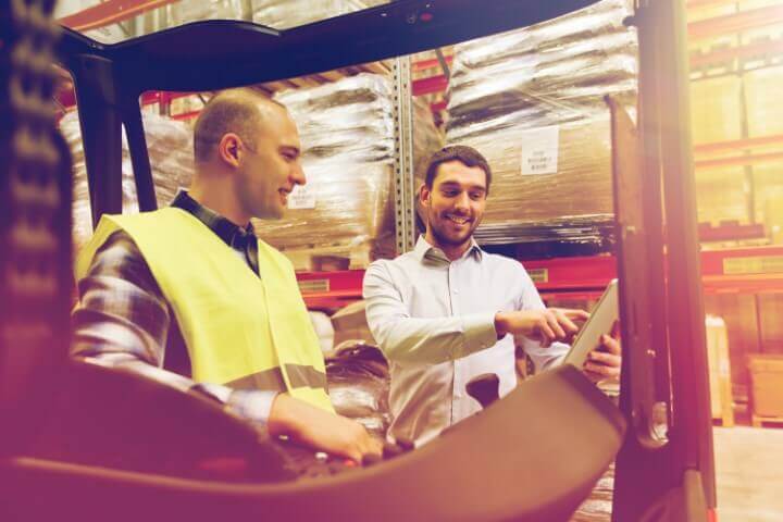 Happy men with a tablet and forklift in a warehouse